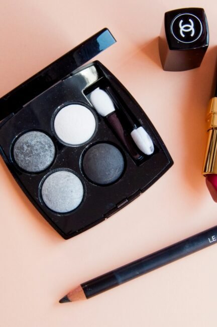 A close-up image of a makeup brush hovering over a vibrant eye-shadow palette, showcasing a variety of rich and tactile powdery textures in realistic detail.